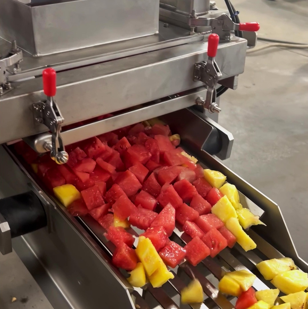 Sliced and diced watermelon and pineapple coming out of an industrial processing cutter and dicer.