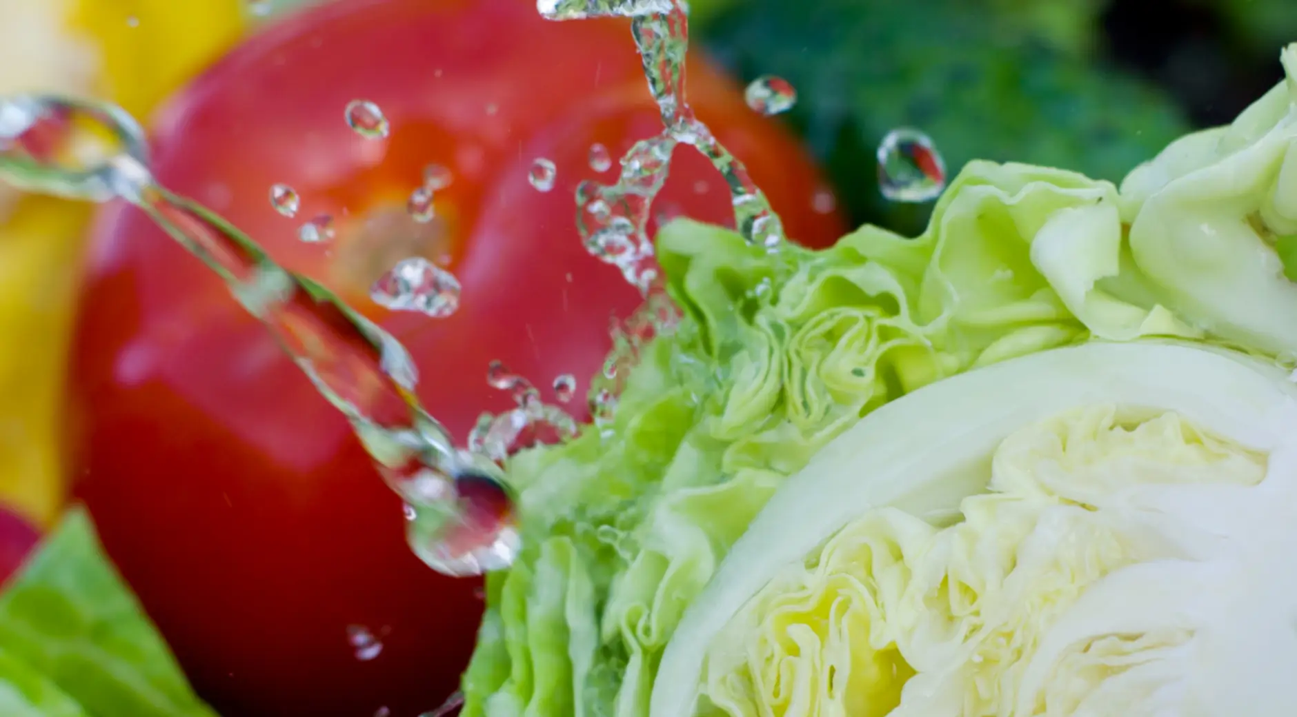 Water spray rinsing fresh vegetables including peppers and leeks during commercial produce washing
